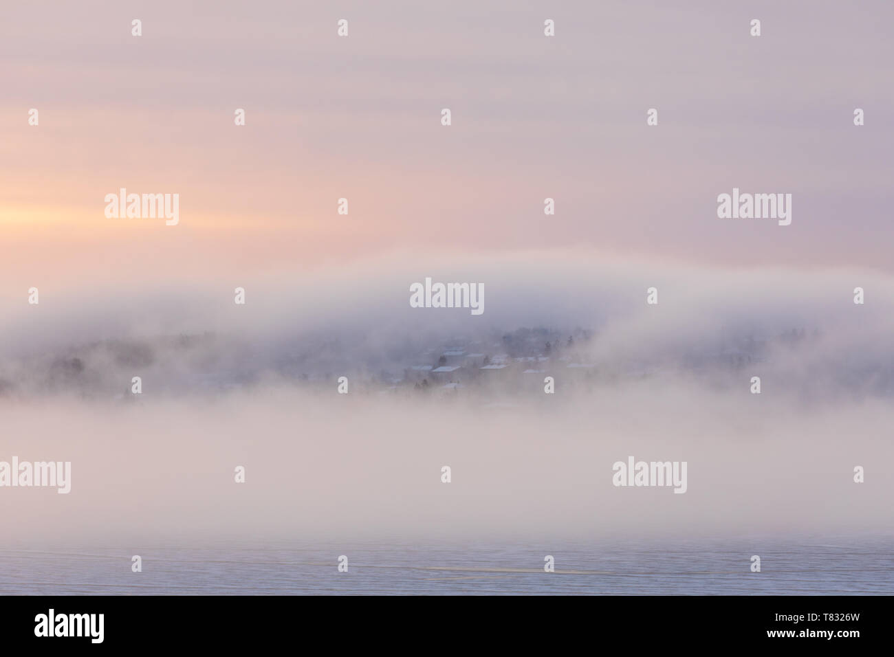 Una fitta nebbia a sunrise oltre la collina e gli edifici della città Foto Stock