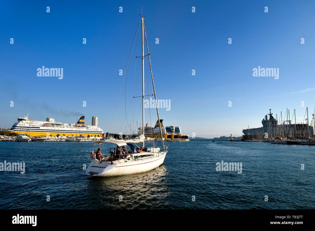Francia, Var, Tolone, una barca a vela lascia il porto, due barche di Corsica Ferries e il Dixmude (L9015) della Marina nazionale della classe Mistral in background Foto Stock