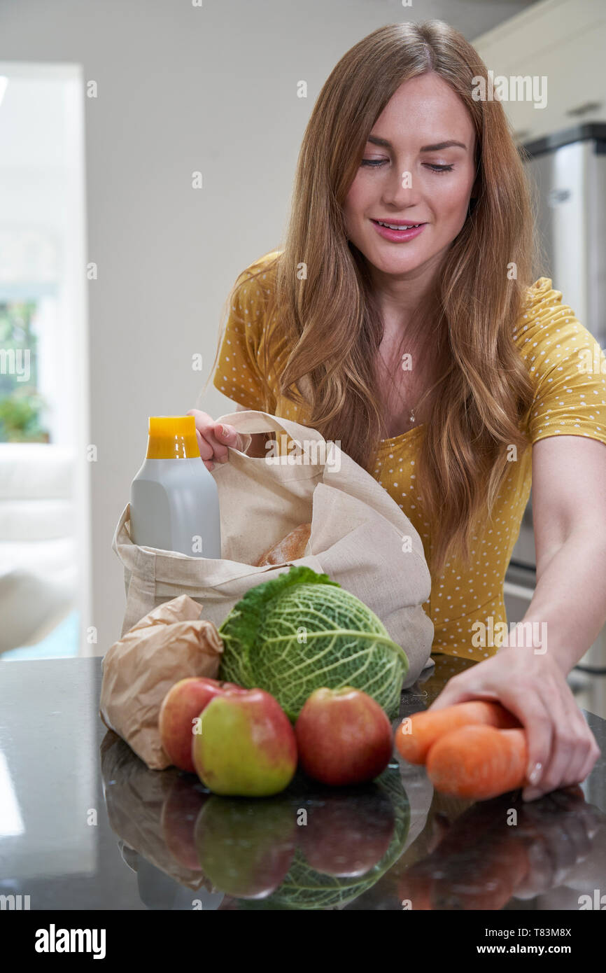 Donna tornando a casa dal viaggio di shopping disimballaggio libera di plastica Sacchi di negozi di generi alimentari Foto Stock