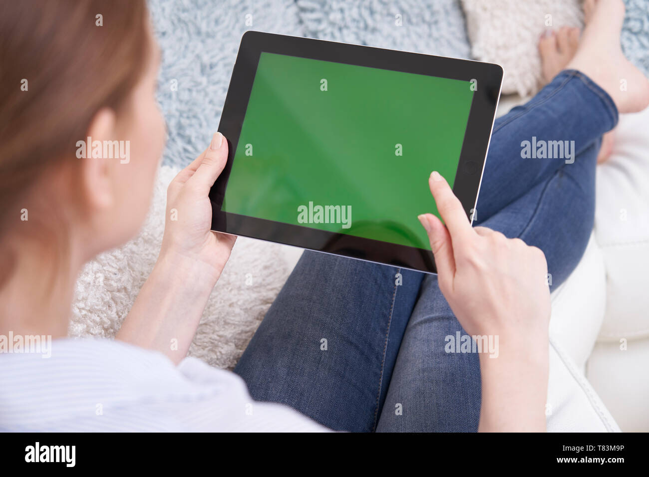 Al di sopra della spalla della donna sdraiata sul divano con schermo verde tavoletta digitale in casa Foto Stock