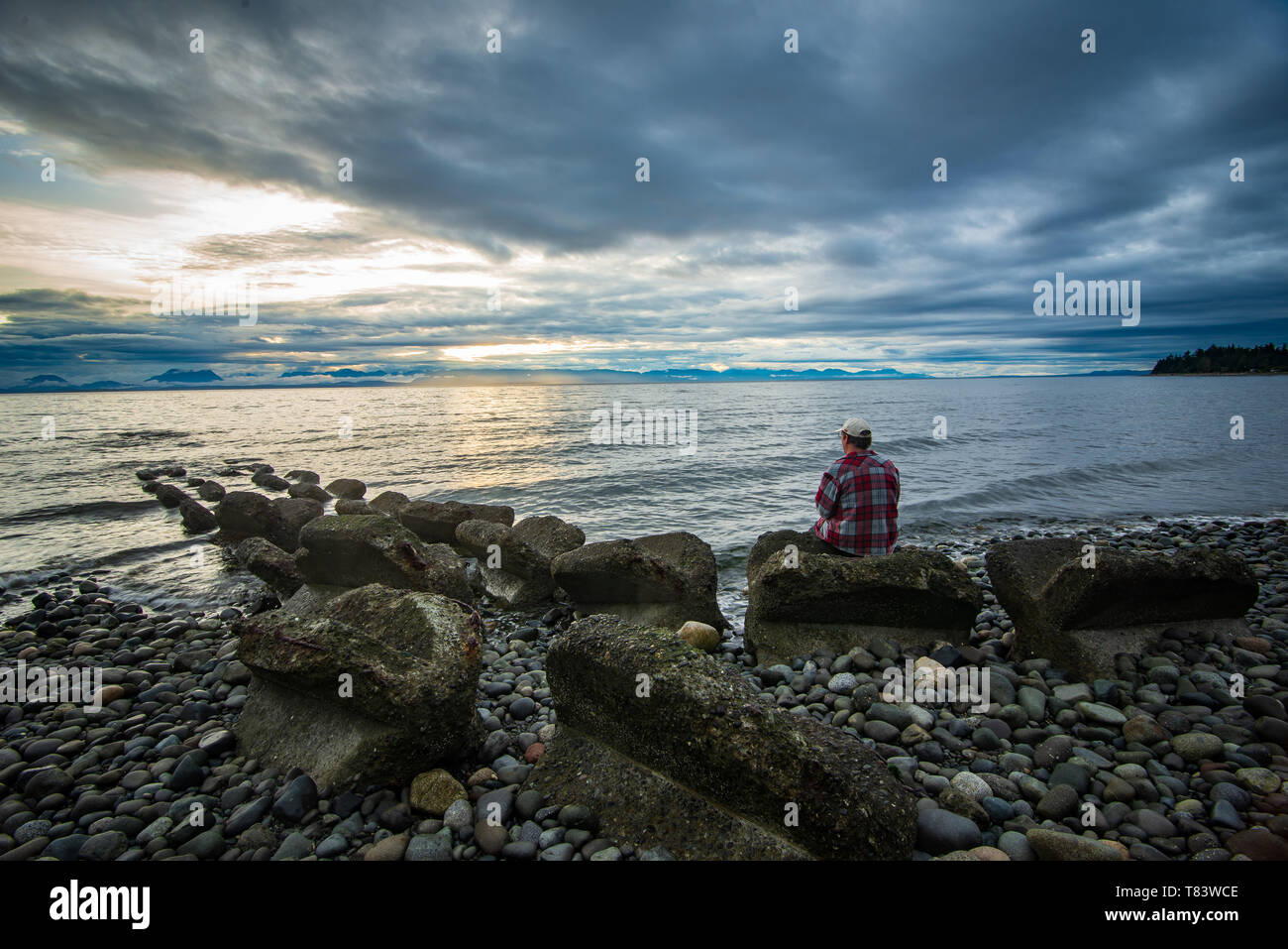 Uomo seduto sul miracolo della spiaggia in Comox Valley, British Columbia, Canada Foto Stock