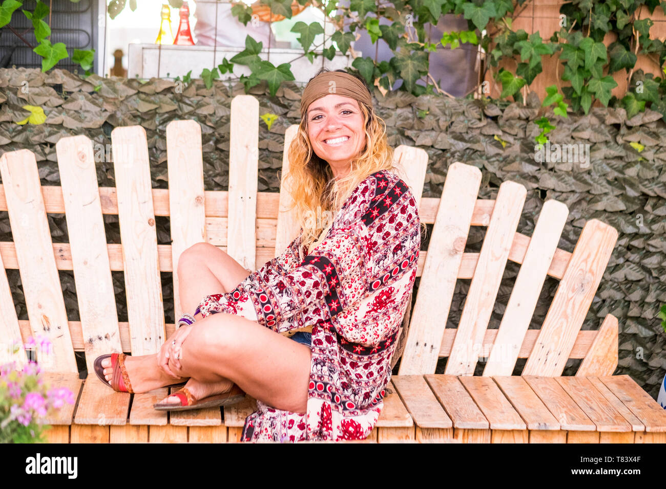 Ritratto di Allegro bella bionda giovane donna seduta su un pallet artigianali panca in legno e guardando la telecamera per esterno Foto Stock