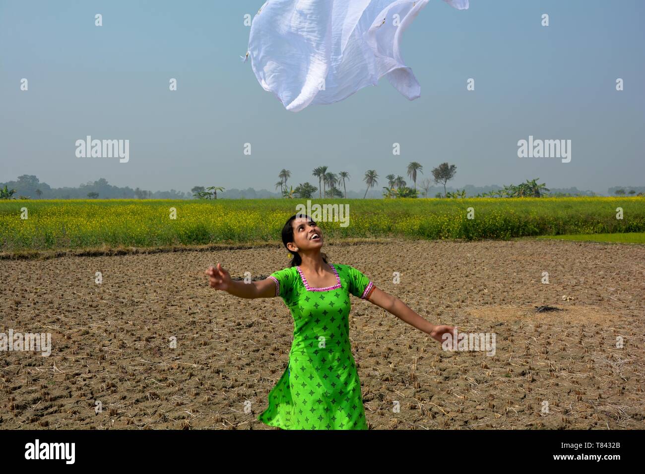 Una ragazza che indossa un salwar kameez battenti un dhupatta bianco / clothin l'aria in un campo su un luminoso giorno, messa a fuoco selettiva Foto Stock