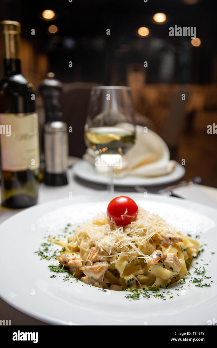 Pasta cremosa con pollo e formaggio servita nel profondo con piastra di vetro bianco vino. Il cibo italiano Foto Stock