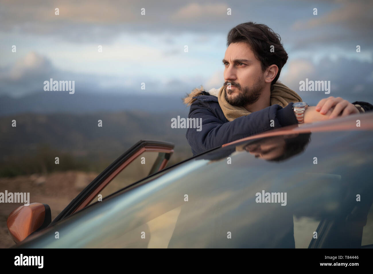 Uomo appoggiato contro auto sulla strada, godendo della vista sulla collina Foto Stock