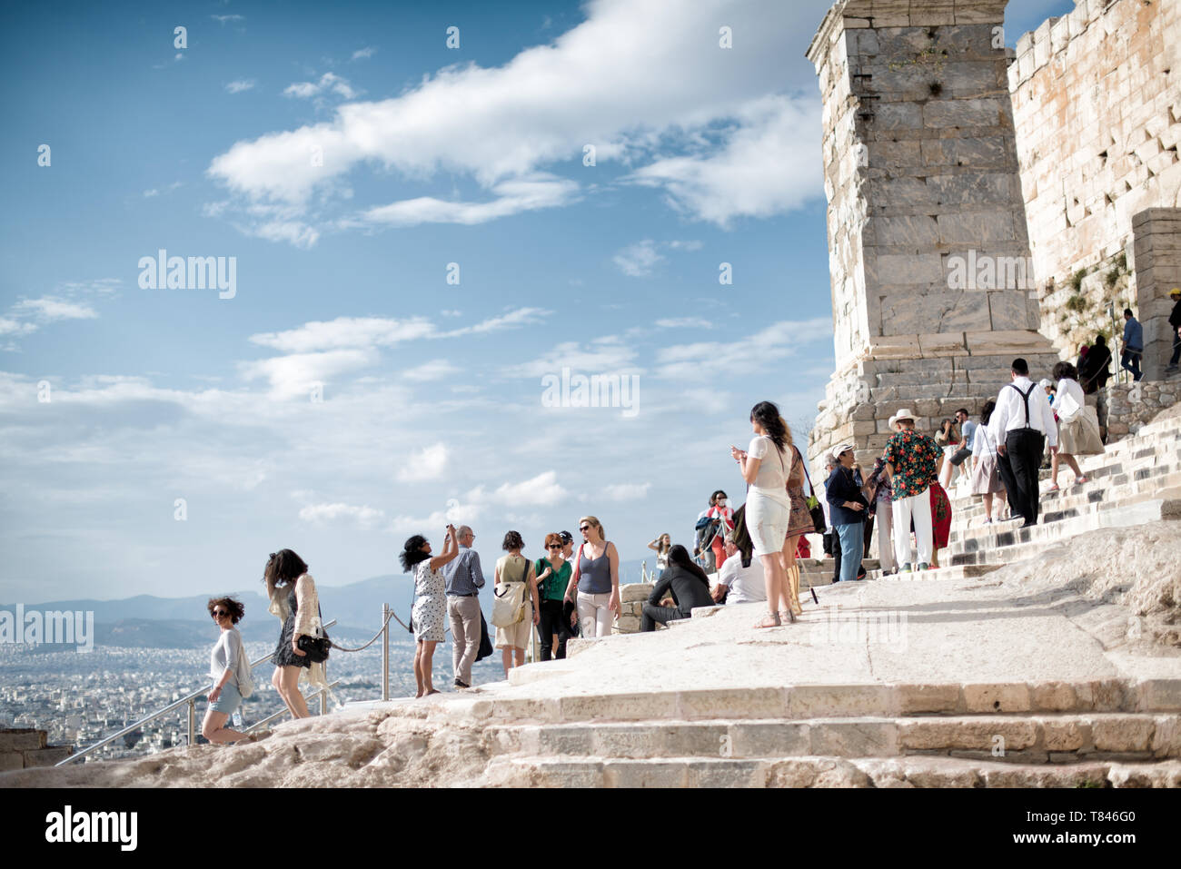 Acropoli con turisti Atene Grecia // ATENE, Grecia - l'antica Acropoli si erge in cima alla sua collina rocciosa, che domina lo skyline di Atene, Grecia. Il Partenone, con le sue colonne e frontoni iconici, è il fulcro di questo sito patrimonio dell'umanità dell'UNESCO. Circondata da altre strutture classiche, tra cui l'Eretteo e il Tempio di Atena Nike, questa cittadella del V secolo a.C. incarna la gloria dell'antica civiltà e dell'architettura greca. Foto Stock