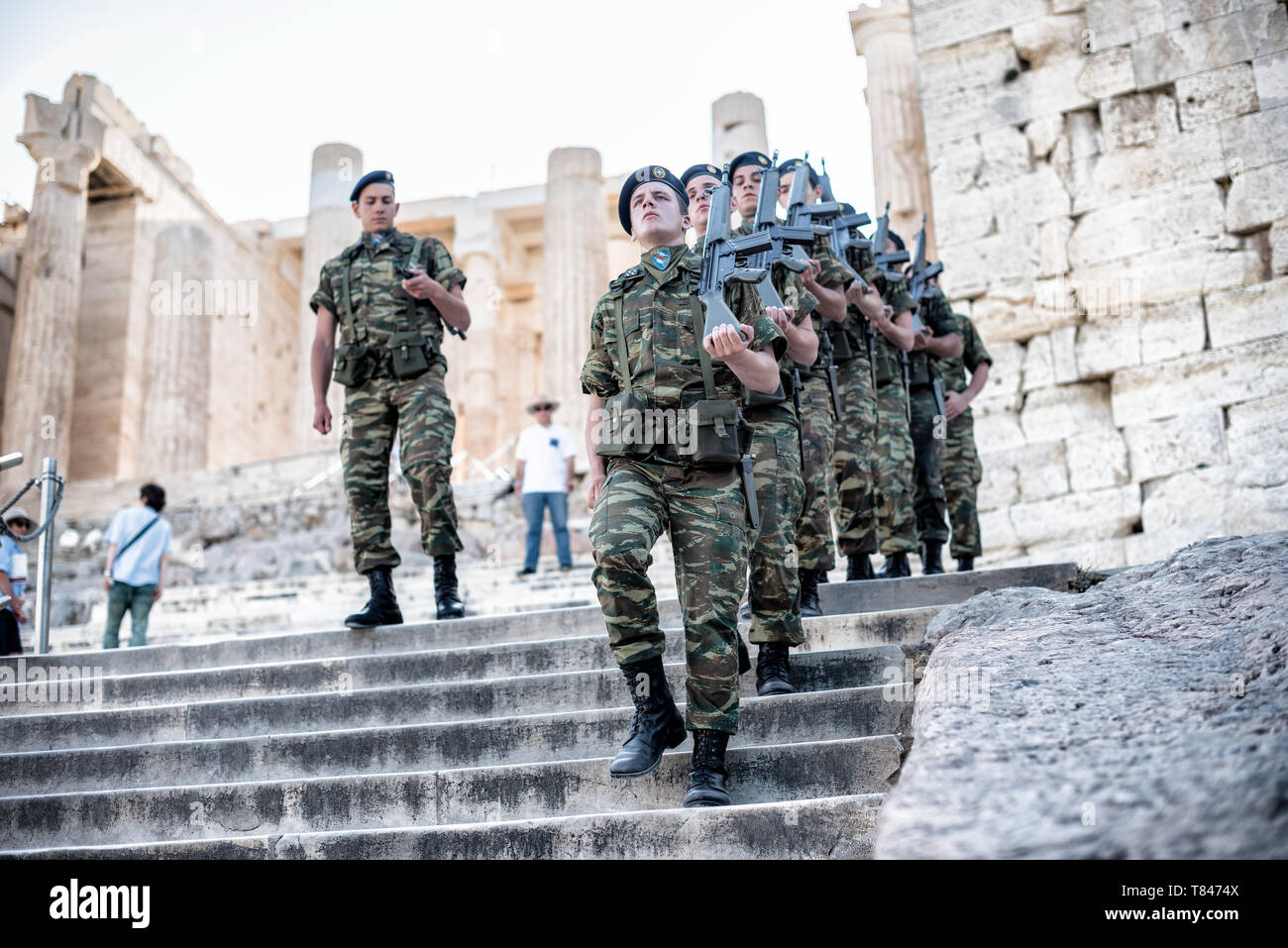 Acropoli soldati greci in formazione di marcia Partenone Atene Grecia | ATENE — Soldati greci scendono i gradini di marmo davanti ai Propilei, il portale monumentale dell'Acropoli, con i fucili in posizione di trasporto. I Propilei furono costruiti dall'architetto Mnesicle tra il 437 e il 432 a.C., combinando colonnati dorici esterni e ionici interni in marmo pentelico, e furono lasciati incompiuti quando la guerra del Peloponneso interruppe il finanziamento del programma edilizio pericleo. Foto Stock