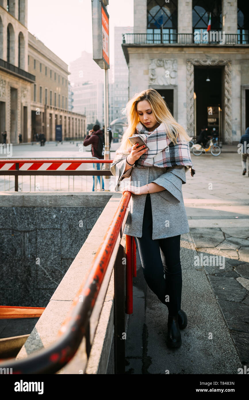 Giovane donna dalla stazione metropolitana di guardare lo smartphone, Milano, Italia Foto Stock