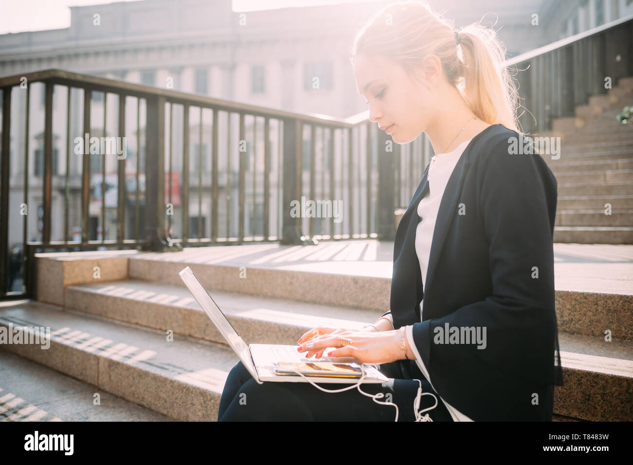 Giovane donna seduta sulla scalinata della città digitando su laptop Foto Stock