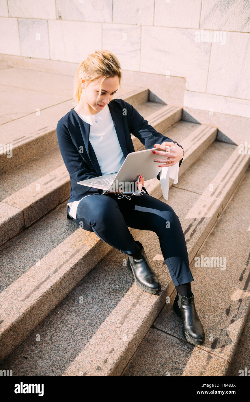 Giovane donna seduta sulla scalinata della città guardando al laptop Foto Stock