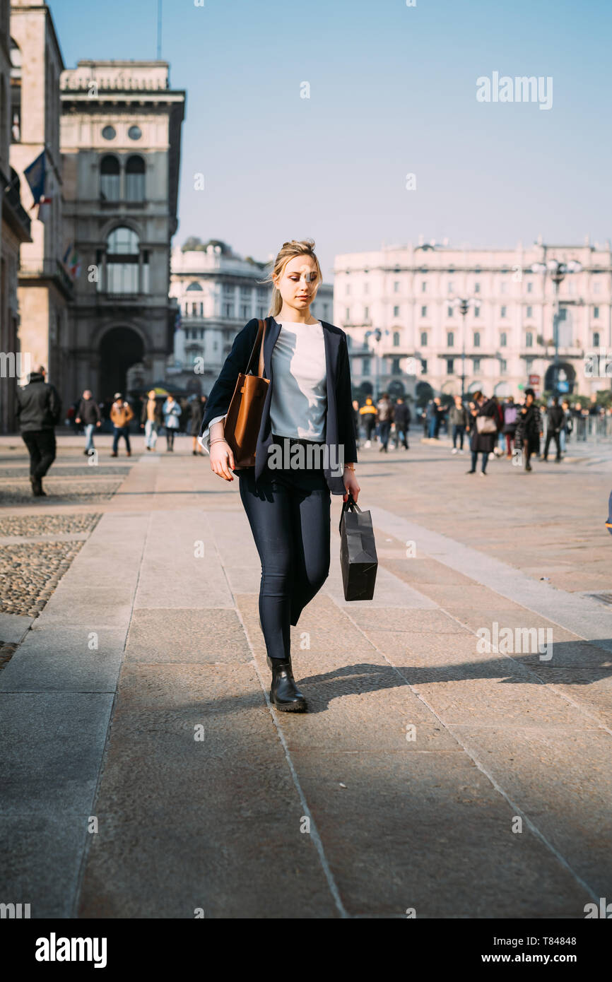 Giovane turista femminile con borse per lo shopping passeggiando nella piazza della città di Milano, Italia Foto Stock
