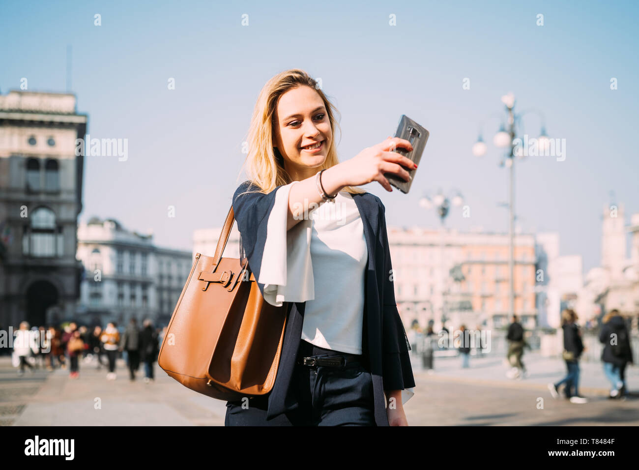 Giovani femmine turistica prendendo selfie dello smartphone in city square, Milano, Italia Foto Stock