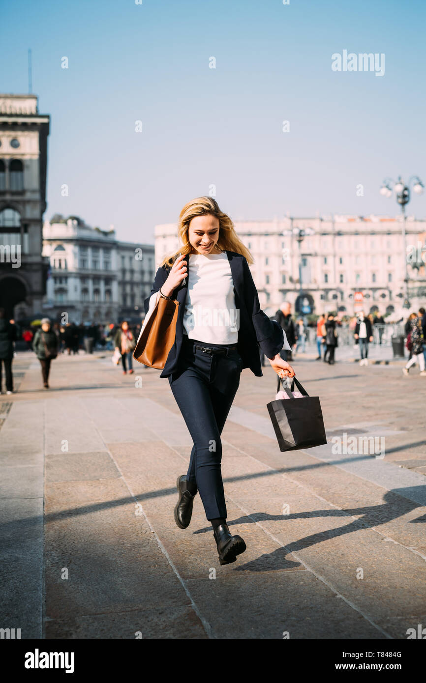 Giovane turista femminile con borse per lo shopping passeggiando nella piazza della città di Milano, Italia Foto Stock
