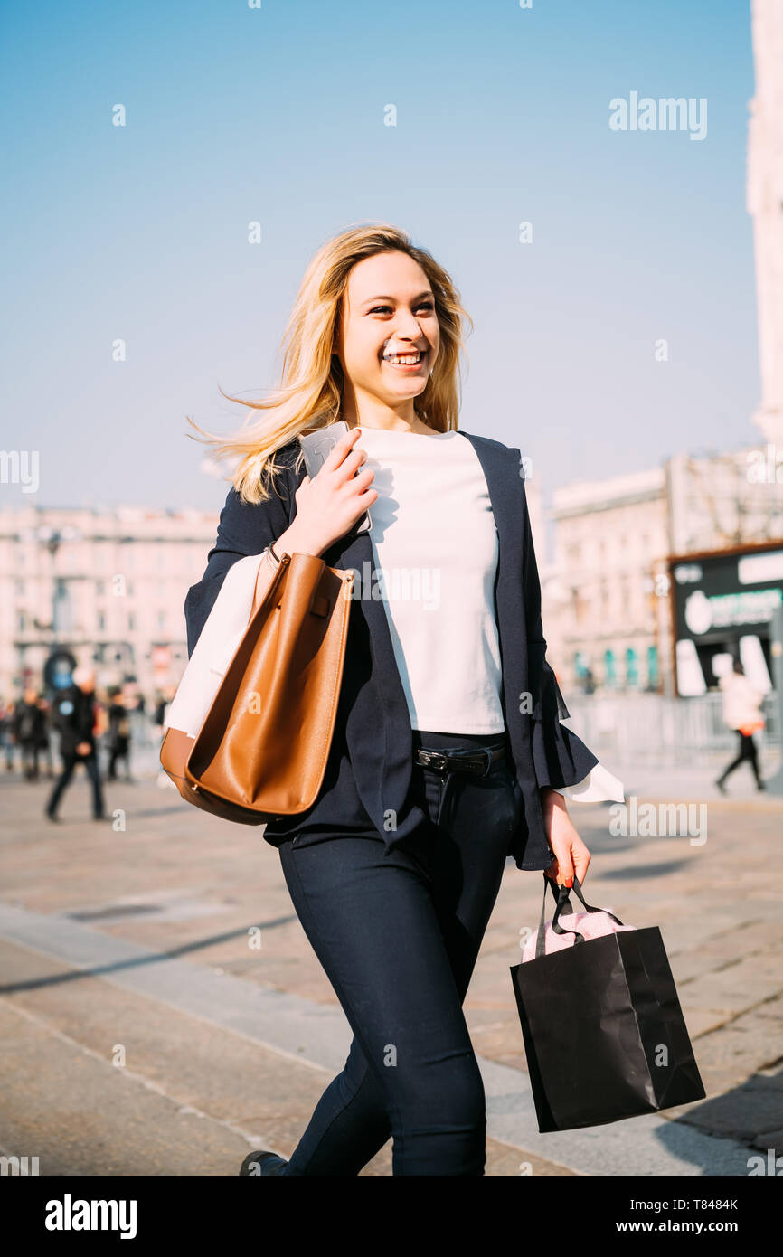 Giovane turista femminile il trasporto delle borse della spesa passeggiando nella piazza della città di Milano, Italia Foto Stock