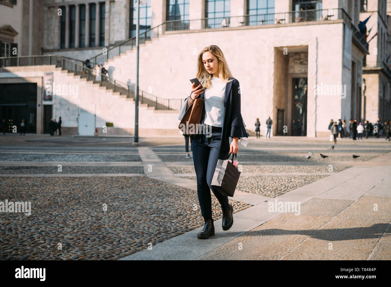 Giovane donna passeggiando nella piazza della città guardando smartphone Foto Stock