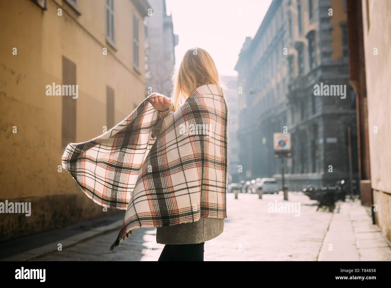 Giovane turista femminile incarto di se stessa in scialle, vista laterale, Milano, Italia Foto Stock