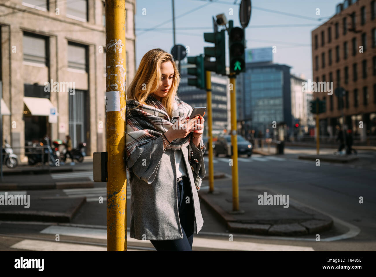 Giovane turista femminile guardando smartphone a stazione del tram, Milano, Italia Foto Stock