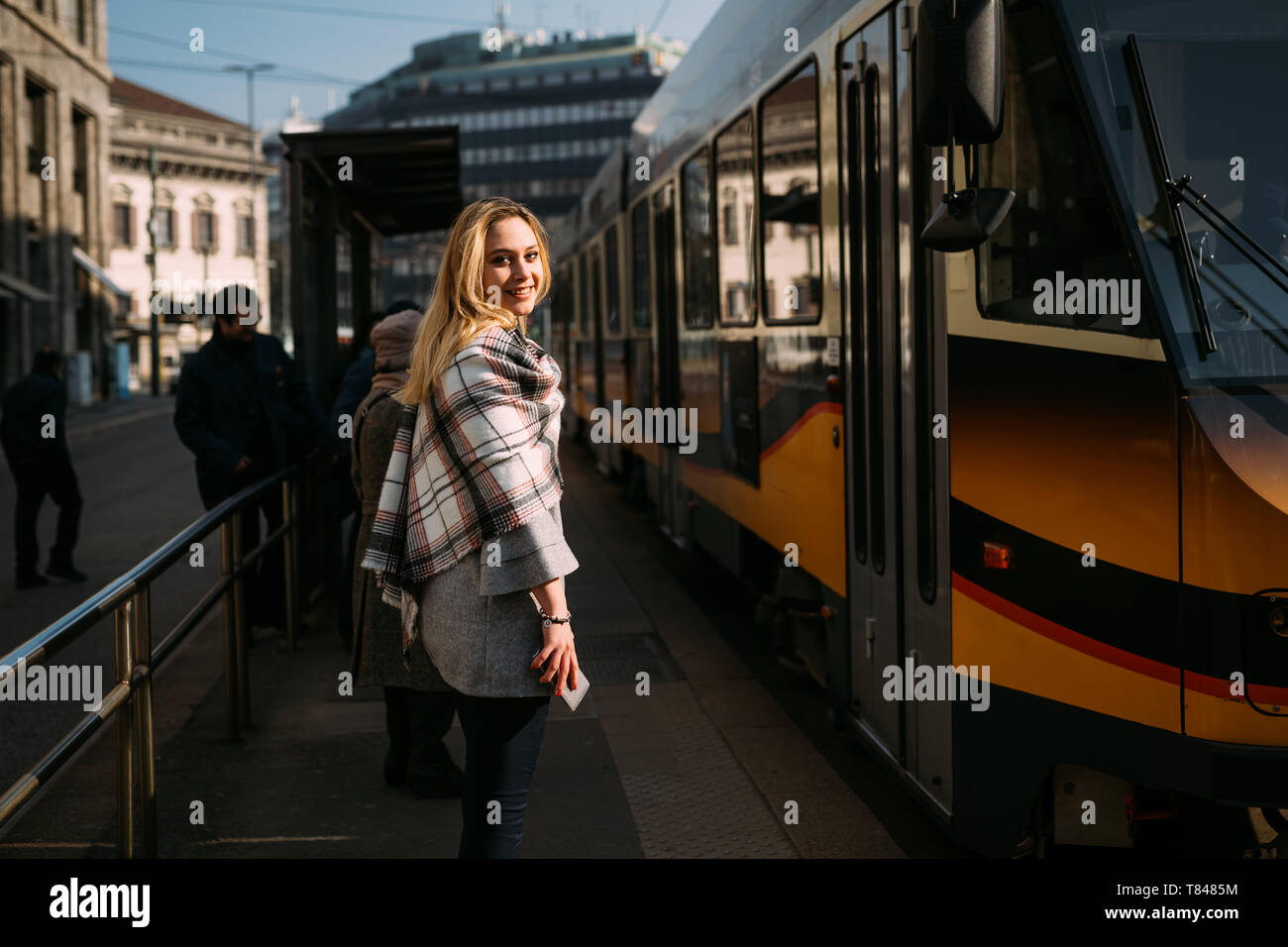 Giovane donna guardando sopra la sua spalla alla stazione del tram, ritratto, Milano, Italia Foto Stock
