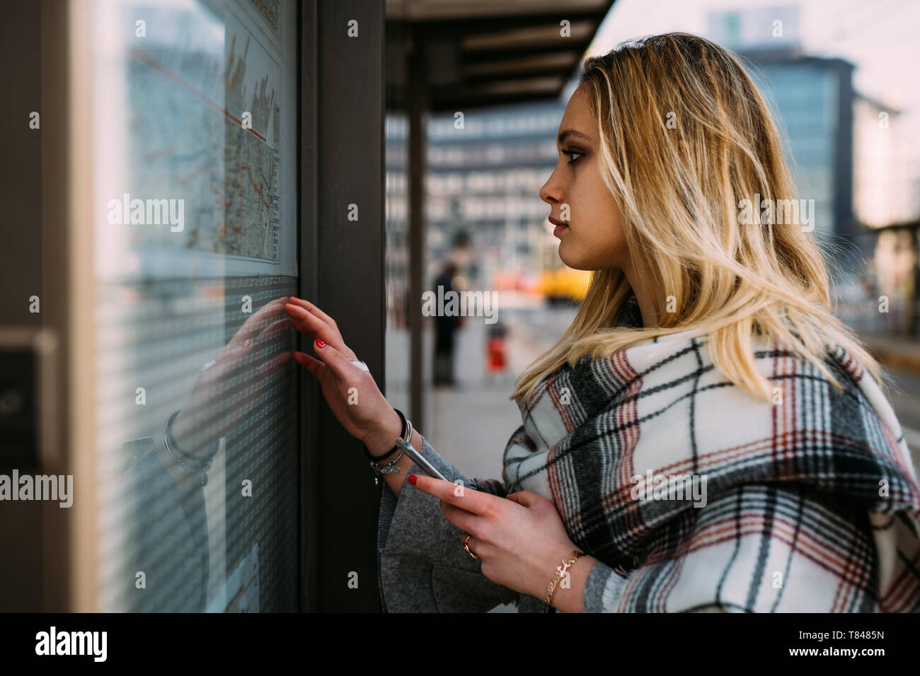 Giovane donna guardando il calendario alla stazione del tram, Milano, Italia Foto Stock
