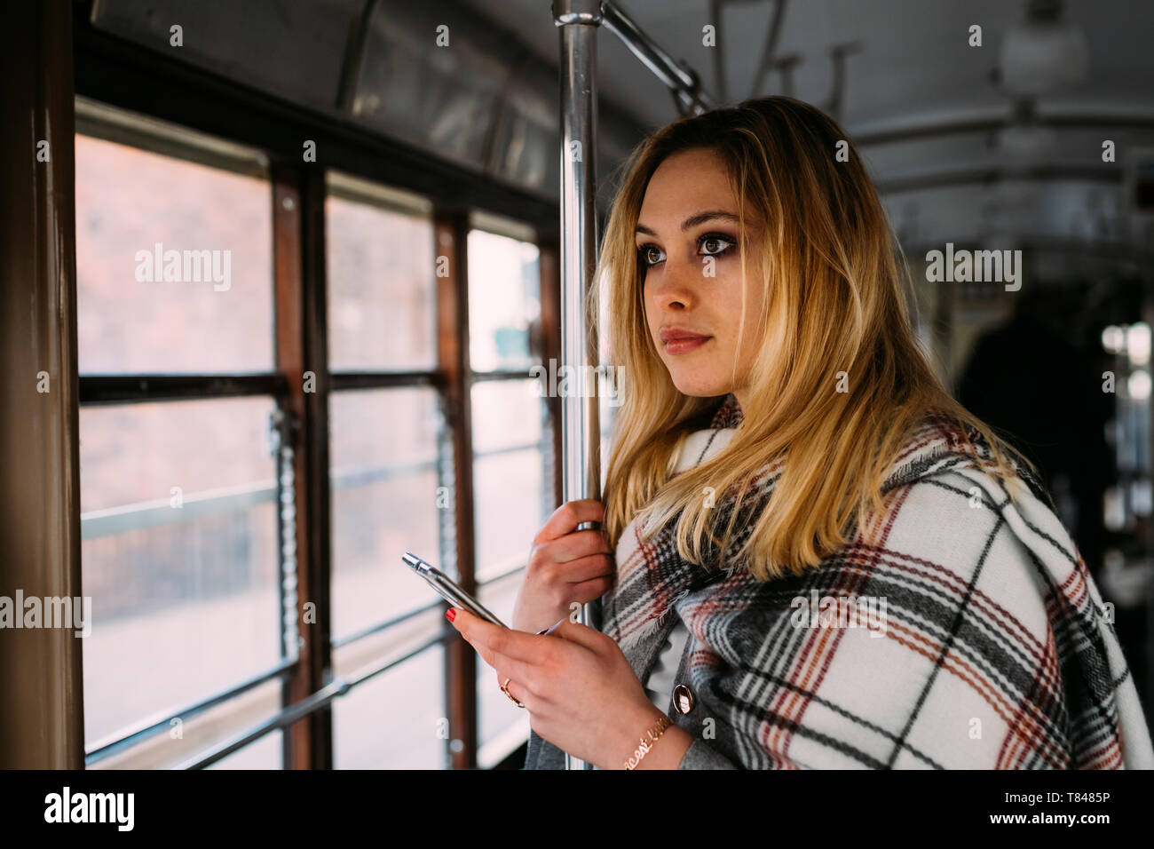 Giovane donna con lo smartphone guardando fuori dalla città il tram Foto Stock