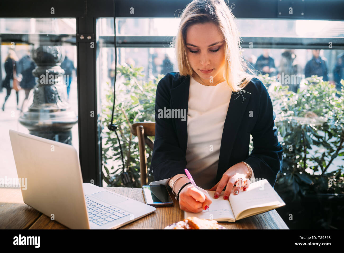 Giovane donna al cafè sul marciapiede di scrittura della tabella nel notebook Foto Stock