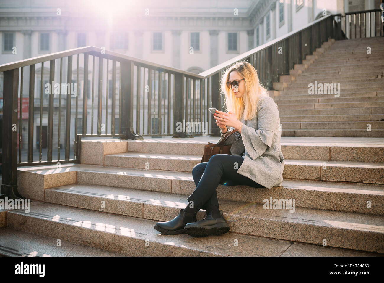 Giovane donna seduta sulla scalinata della città guardando smartphone, Milano, Italia Foto Stock