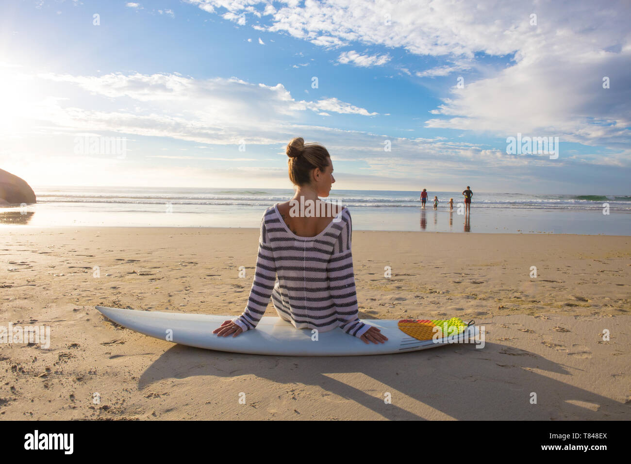 Surfista femmina seduto sulla tavola da surf in spiaggia, vista posteriore, Cape Town, Western Cape, Sud Africa Foto Stock