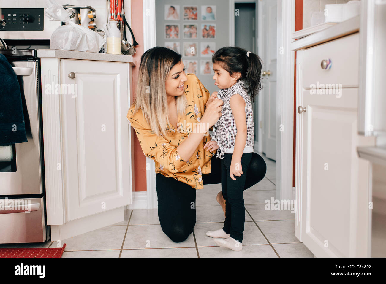La ragazza madre il suo fissaggio camicetta pulsanti in cucina Foto Stock