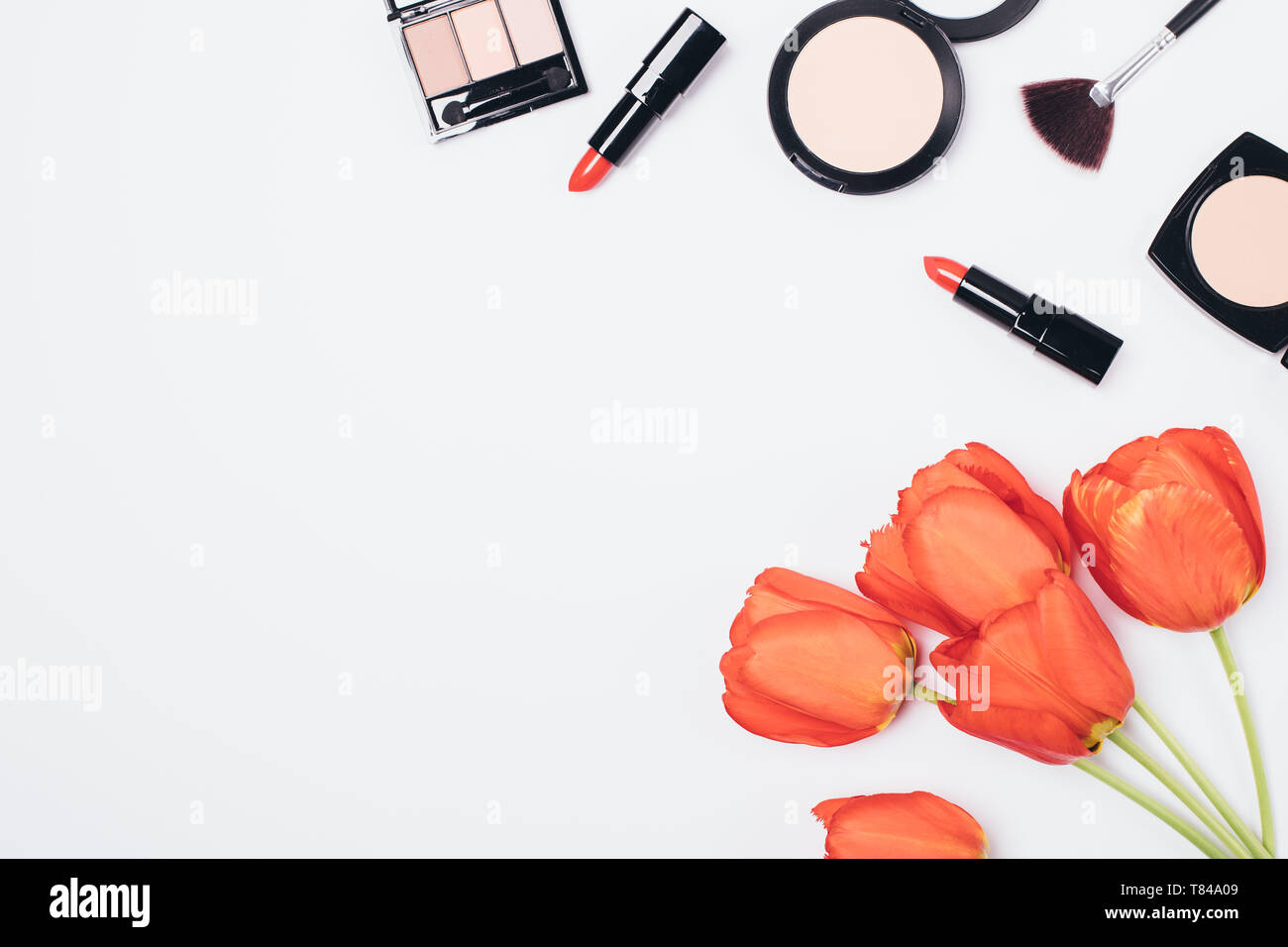 Piatto disposizione laici delle donne di prodotti cosmetici per il trucco e accessori bouquet di tulipani rossi su sfondo bianco con copia spazio, vista dall'alto. Foto Stock