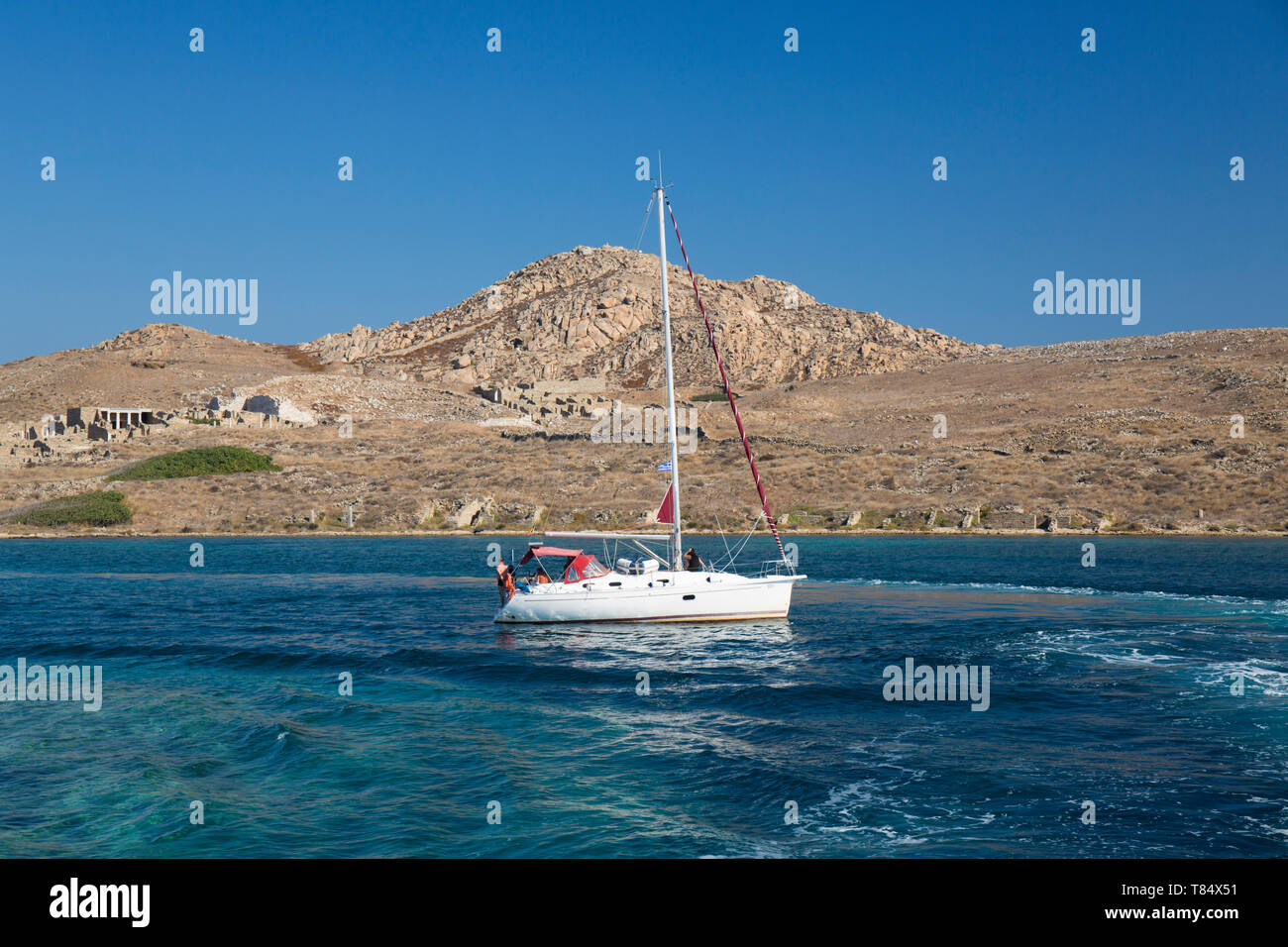 Delos, Mykonos, Egeo Meridionale, Grecia. Yacht a vela attraverso il canale di Delos, il Delos sito archeologico visibile sullo sfondo sotto il monte Kynthos. Foto Stock