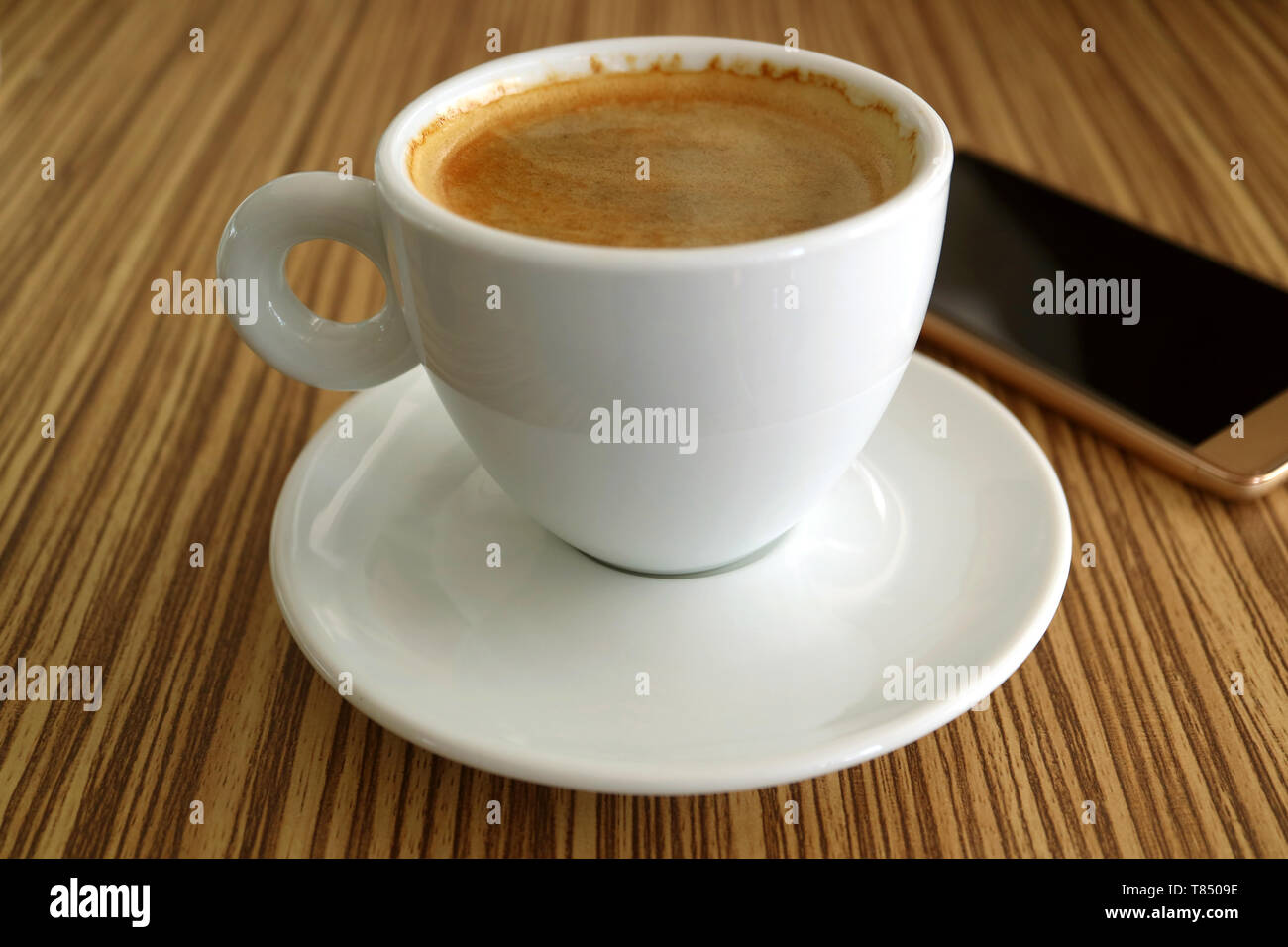 Una tazza calda di caffè nero con un Smartphone sfocate in background Foto Stock