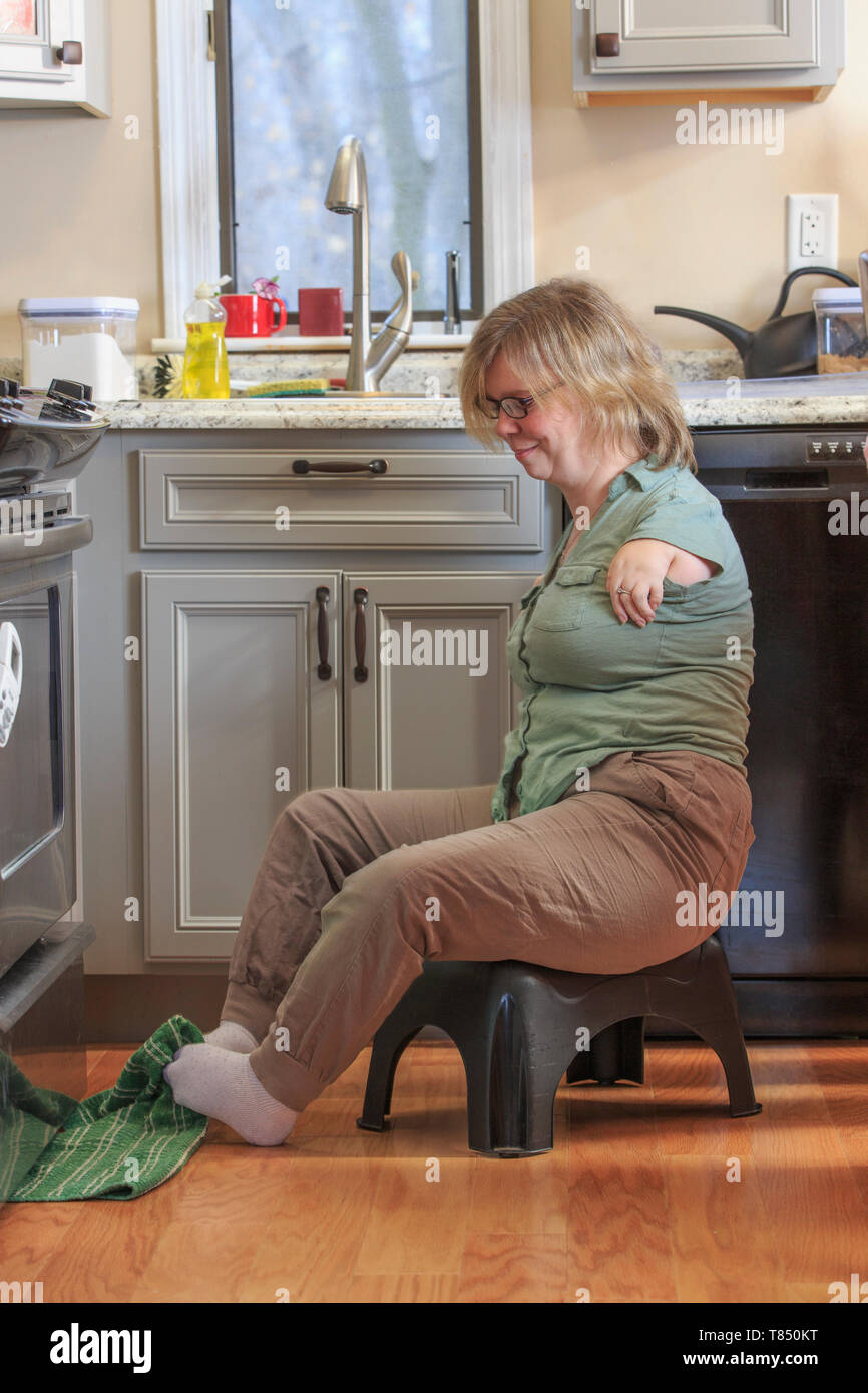 Donna con sindrome di catrame di prelevare un asciugamano da cucina con i suoi piedi Foto Stock