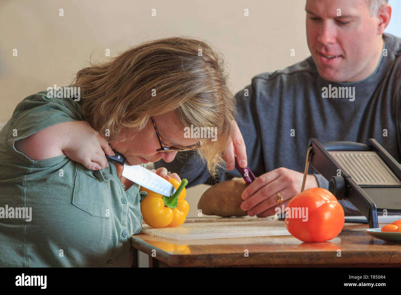 Donna con sindrome di catrame come tagliare le verdure con il marito in cucina Foto Stock