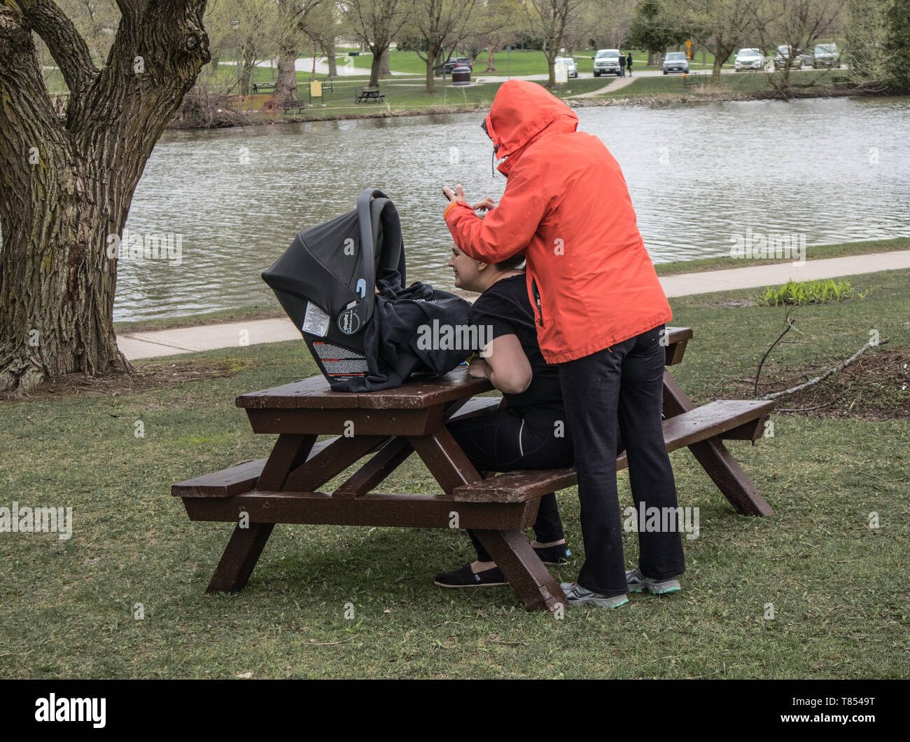 Due donne e un bambino nel parco di Stratford, Ontario. Uno di loro prende una foto del bambino. Cool grey giorno. Foto Stock