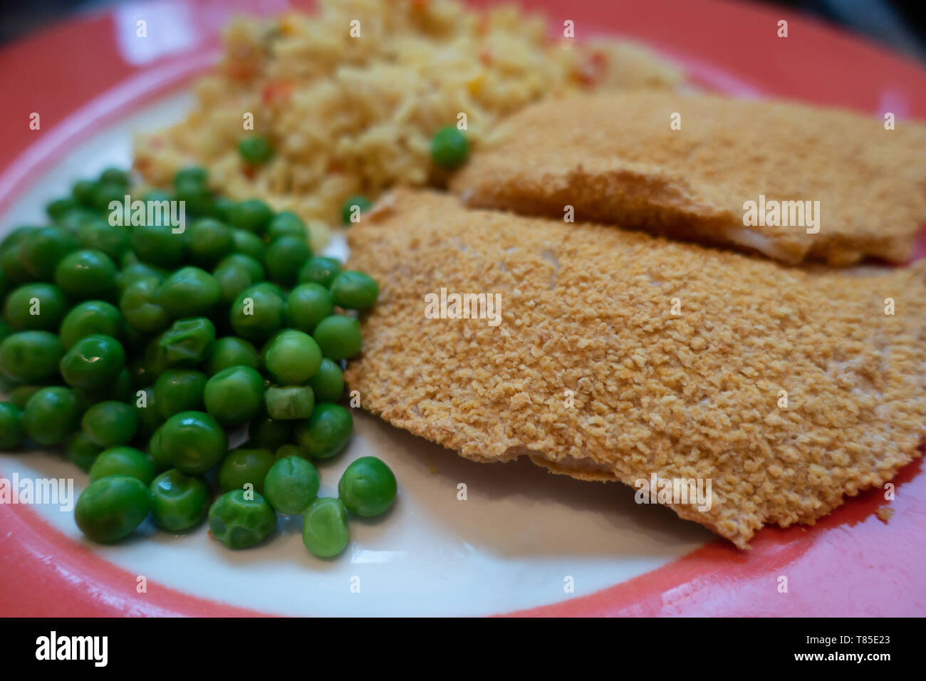 Findus croccanti frittelle cucinate e servite con piselli e aromatizzata riso su una targhetta rossa. Foto Stock