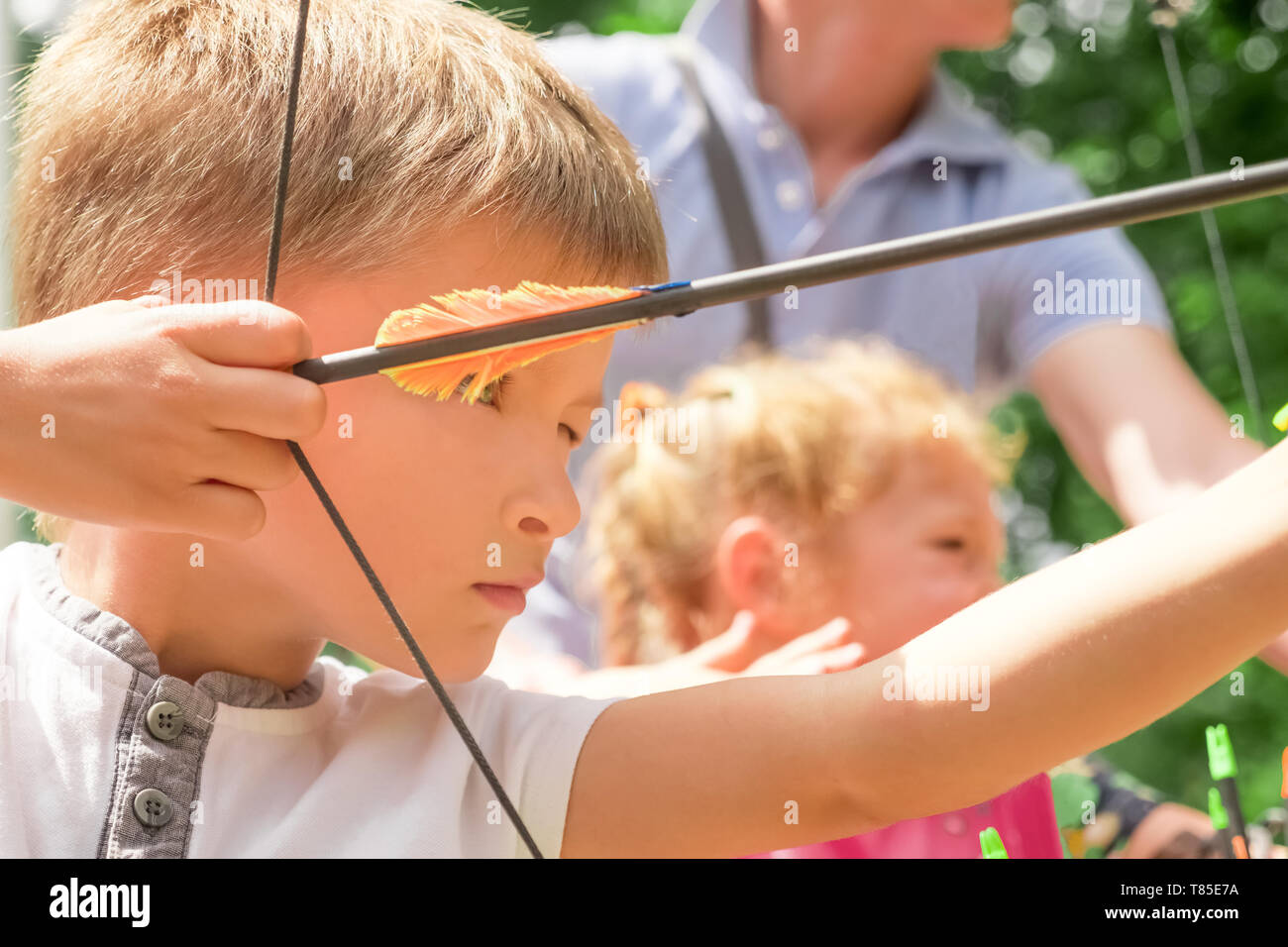 Ragazzo con arco e frecce concentrato sul bersaglio. Ragazzo carino con un arco e frecce. Bambini e sport. Allenamento fisico. Bowman sfondo. Foto Stock