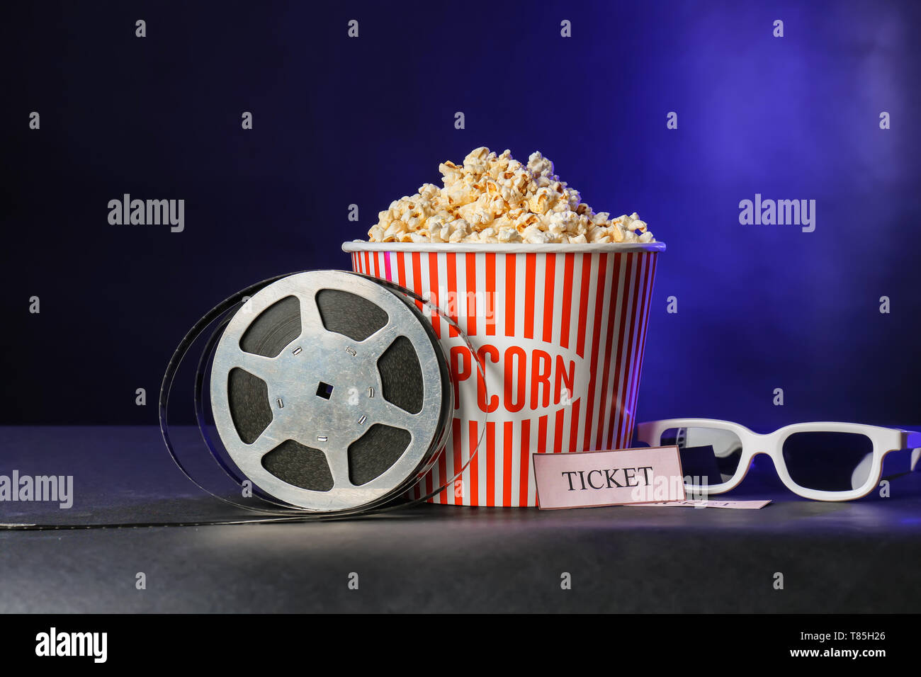 Benna con gustosi di popcorn e bobina di pellicola su sfondo scuro Foto Stock