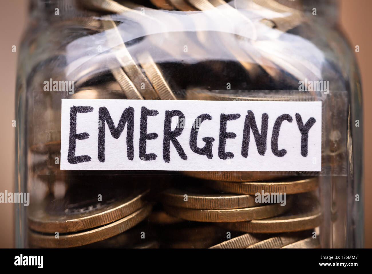Monete in vaso con etichetta di emergenza sulla scrivania in legno Foto Stock