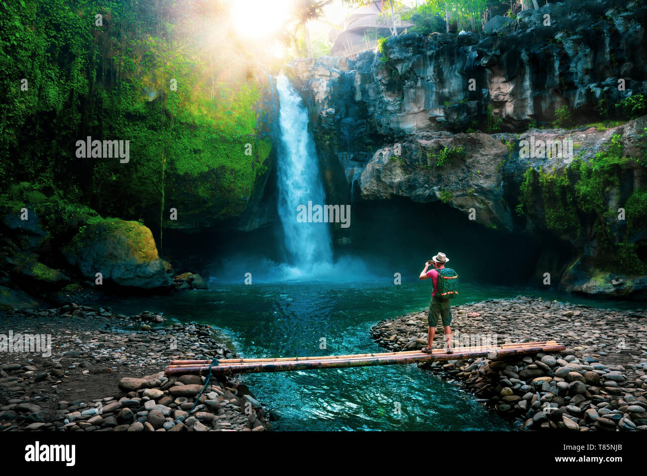 Uno stile di vita attivo fotografo di viaggio con la macchina fotografica e uno zaino fare foto cascata nascosta in una giungla tropicale Foto Stock