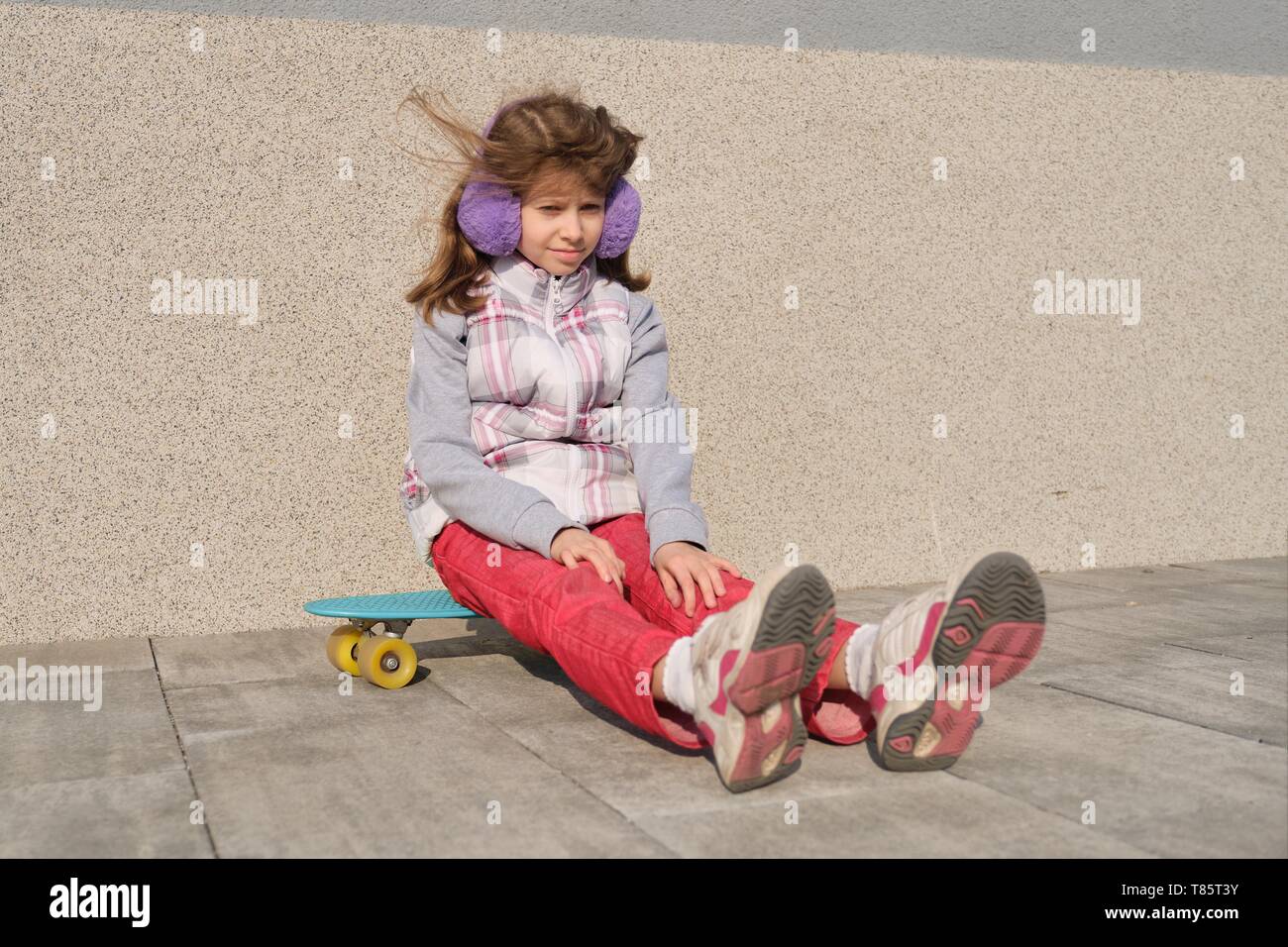 Bambina rides uno skateboard, nella zona vicino alla casa, stagione primaverile, muro grigio Sfondo. Foto Stock