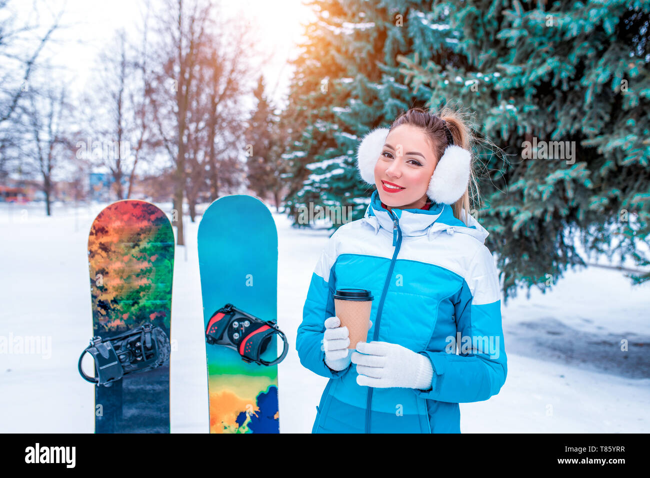 Felice donna sorridente, inverno al resort nel mezzo di neve e abeti. Snowboard, tazza di tè del caffè. Bella ragazza in una calda tuta sportiva. Spazio libero Foto Stock