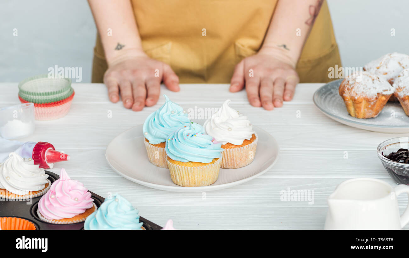 Vista ritagliata della donna vicino a tavola con piastra con gustosi tortini su grigio Foto Stock