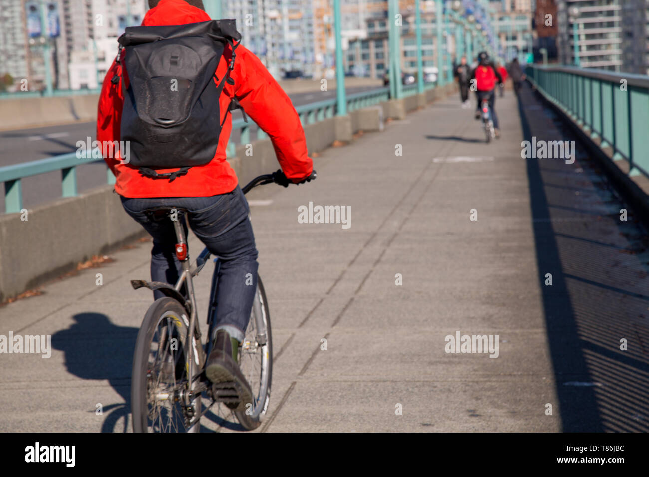 Anonimo ciclista maschio giacca rossa zaino nero sella città moderna Foto Stock