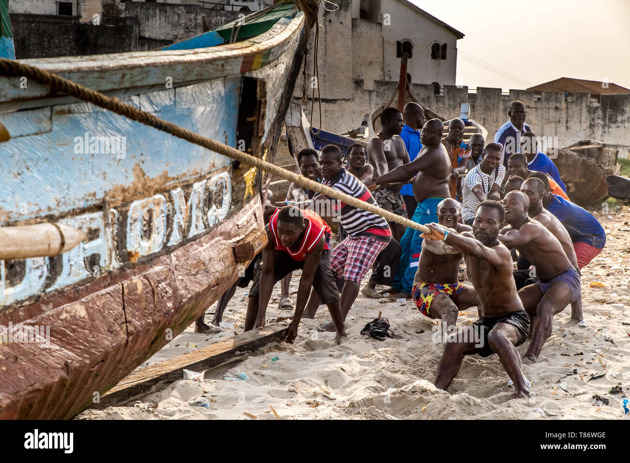 Un gruppo di uomini trascina una barca da pesca fuori dall'acqua in una spiaggia a Cape Coast, Ghana. Foto Stock