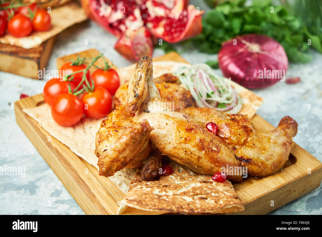 Pollo alla griglia su una tavola di legno con le verdure su uno sfondo grigio Foto Stock