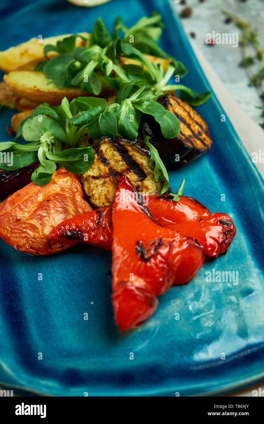 Grigliata di verdure e patate rustiche su un bel piatto di colore blu su sfondo grigio Foto Stock