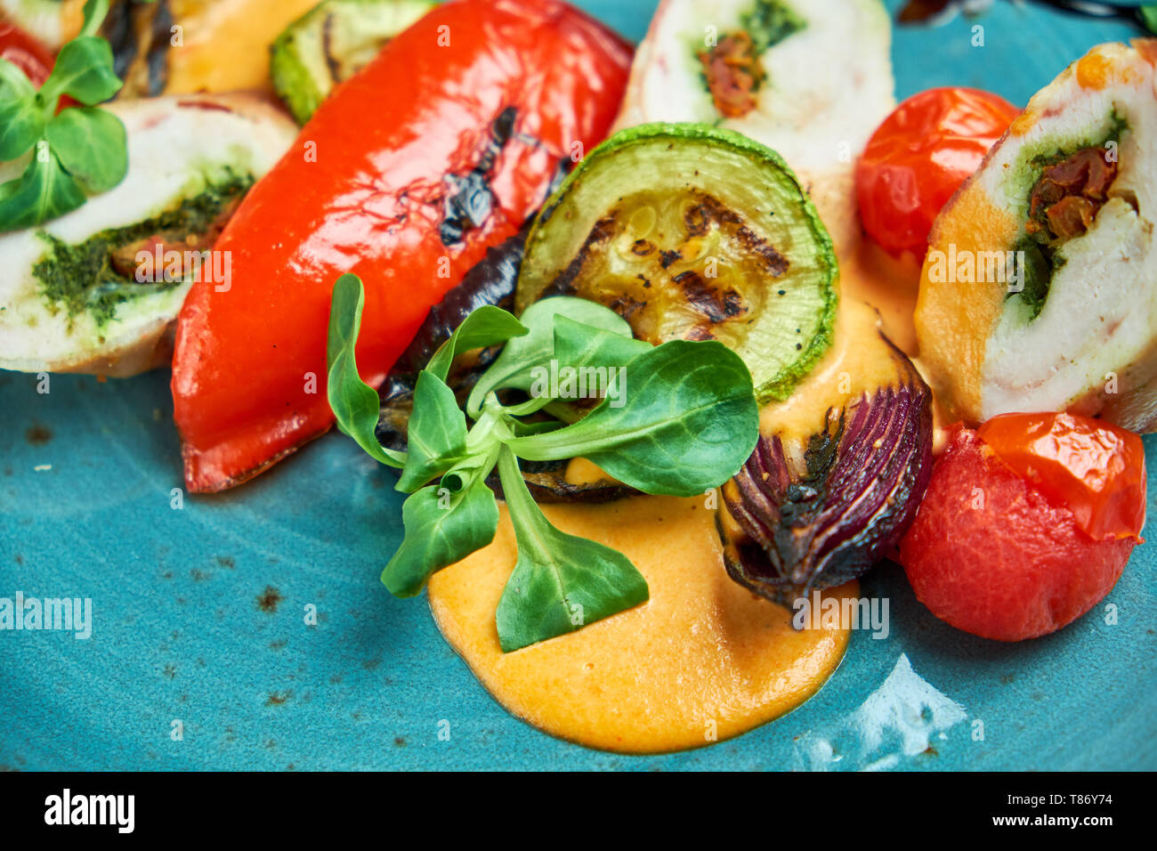 Involtini di pollo farcito con spezie con verdure alla griglia su un bel piatto di colore blu su sfondo grigio Foto Stock