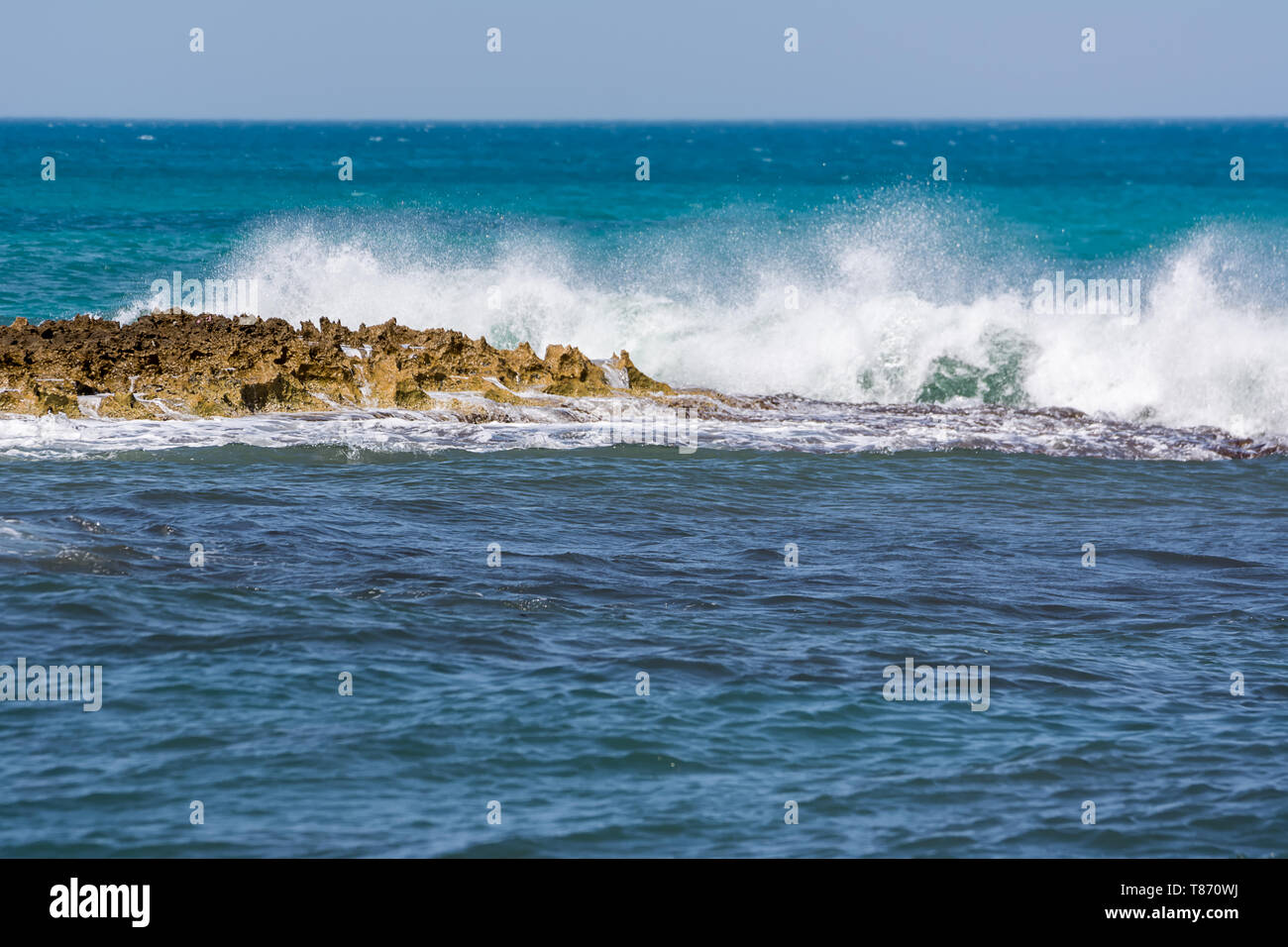 Onde spumeggianti che si infrangono sulla costa rocciosa e il mare blu Foto Stock