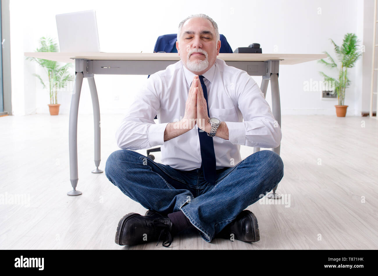 Imprenditore invecchiato facendo esercizi yoga in ufficio Foto Stock