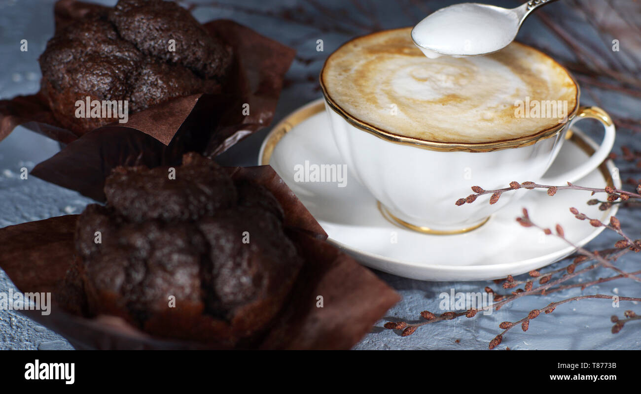 Una tazza di caffè cappuccino sorge sul tavolo accanto a due bellissimi muffin al cioccolato Foto Stock